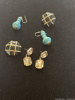 Top-down photo showing four pairs of vintage earrings arranged on black background including amber-colored gemstone dangles, turquoise bead dangles, gold-tone grid domed clip-ons, and amber-colored studs.