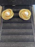 Close up photo of the pair of vintage earrings showing the central faux pearl and twisted rope gold tone design on black background.