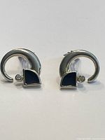 Photo of vintage crescent-shaped earrings in silver-tone metal with clear rhinestone and black enamel triangle detail, presented on white background.