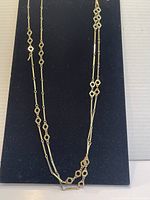 Front view of the gold plated long chain necklace displayed on navy blue backing, showing the full length and intricate geometric links.