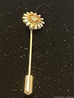 Full length view of the brooch pin showing the flower head with crystal center and the long gold plated pin with clutch end.