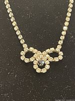 Clear rhinestone necklace with a black central stone forming a decorative bow-like design on black background.