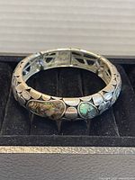 Front and angled view of the silver-tone bangle bracelet showing shell inlays and metal segment design.