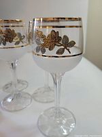 Close-up of single glass showing gold floral band and frosted section