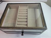 Closed jewelry box showing glass panels, metal frame, drawer knob