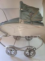 Side view of vintage metal baby buggy with green canopy and four wheels