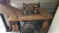 Full view of the antique Singer sewing machine in wooden cabinet showing drawers and folding top section.