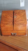 Front view of antique wooden stationery box with two top panels and bottom drawer with metal handle.