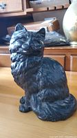 Front angle view of cast iron black cat figurine on wooden surface, showing detailed fur texture and facial features.
