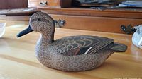 Side view of the hand-carved wooden duck decoy painted in naturalistic colors, detailed feather pattern visible.