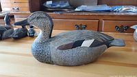 Front-side view of carved duck decoy displaying detailed painted feather pattern and naturalistic colors on a wooden surface.