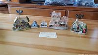 All five David Winter handmade and handpainted houses arranged in a row on a wooden table with Certificate of Authenticity in front