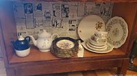 Shelf displaying stacked Royal Doulton and Hammersley plates, teapots, and cups with chips visible on dishes