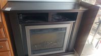 Electric fireplace with dark brown mantel, two open shelves above firebox, and simulated logs in the firebox. Shown from a frontal view with natural lighting.