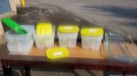 Multiple clear plastic storage containers with green and yellow lids displayed on a wooden surface outdoors