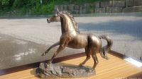 Left side view of bronze horse sculpture on wooden surface with outdoor background.