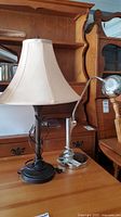Photo showing two lamps on a wooden surface, including a brown twisted column table lamp with beige bell shade and a silver adjustable desk lamp.