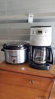 Photo showing Rival crockpot and Cuisinart 12 cup coffee maker side by side on a wooden surface.