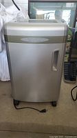 Front view of silver-heavy duty paper shredder with power cord on floor.