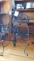 Front view of the black metal folding plant stand with three circular holders with ornamental star and scrollwork accents