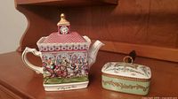 Side view of Sadler teapot and crumb caddy on wooden surface, details of racing scene and floral crumb caddy visible