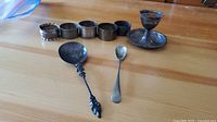 Photo showing the full lot including six napkin rings, two spoons, and one candlestick displayed on a wooden surface.
