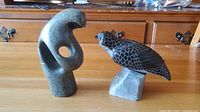 Photo showing both soapstone figurines on a table: one abstract human shape and one bird on a block base.