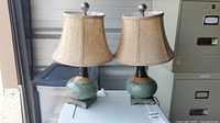 Two pottery-based glazed table lamps with beige fabric shades on a metal accent base, both about 17 inches tall