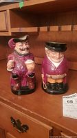 Two Royal Doulton Toby mugs placed side by side on a wooden surface, showing their full figures.