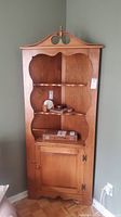 Front view of the maple wood corner cabinet showing all three shelves and lower cabinet door, light wood finish, traditional style.
