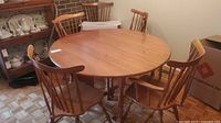 Round wooden drop leaf table with six matching chairs around it, showing warm wood finish and turned legs on table and chairs.