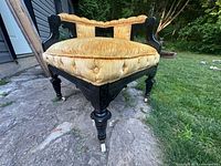 Photo showing front side details of the 19th century corner chair including porcelain castor wheels and tufted mustard yellow upholstery with wood carvings.