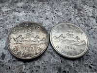Reverse sides featuring canoe scene with two figures and tree on 1952 and 1956 silver dollar coins