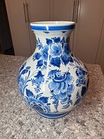 Full view of Delft vase showing round body and detailed blue floral decoration on white ceramic.