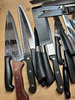 Top-down view of assorted kitchen knives including large chef knives, steak knives, and a comb-like serrated blade