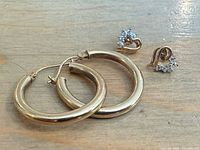 Pair of 10k yellow gold hoop earrings approx. 1" diameter and pair of heart-shaped diamond stud earrings on wooden surface