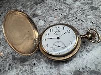 Gold filled Waterbury Watch Company pocket watch with open cover showing white dial, black Arabic numerals, and company logo.