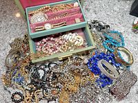 Photo showing the full jewelry box open with various necklaces and bracelets surrounding it on a countertop, demonstrating the assortment and condition of items.