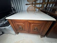 Front and top view showing large white beveled marble top with wooden base featuring panel doors and ring pull handles.