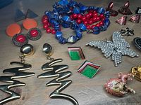 Photo showing two beaded necklaces, multiple pairs of earrings, and brooches arranged on table.