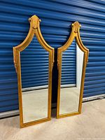 Pair of tall wooden framed mirrors standing side by side showing full front reflective surfaces and shaped tops