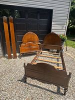 Pair of assembled single beds with headboards, footboards, and rails laid out outdoors on gravel.