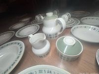 Photo showing teapot, cream pitcher, sugar bowl, and several plates arranged on floor