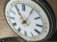 Close-up of white enamel dial showing applied gold-tone geometric and floral markers, black Roman numerals, gold-tone hands