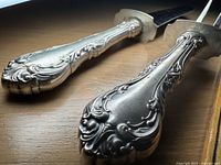 Close-up view of the ornate sterling silver handles on the carving knife and fork showing intricate scroll and floral design.