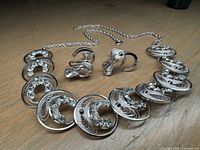 Full view of the sterling silver necklace and matching earrings arranged on a wooden surface, highlighting rhinestones and engraved details.