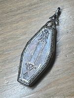 Front view of coffin-shaped sterling silver pendant locket showing engraved floral design and rectangular cartouche area.