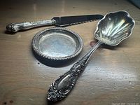 Three sterling silver pieces (serving spoon, coaster, cake knife) laid out on wood surface