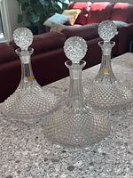 Three clear glass decanters arranged on a granite countertop, showing hobnail pattern and ball stoppers. Two have original labels visible on the bodies.