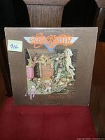 Front cover of Aerosmith 'Toys in the Attic' vinyl album showing vintage toy attic artwork and band logo.